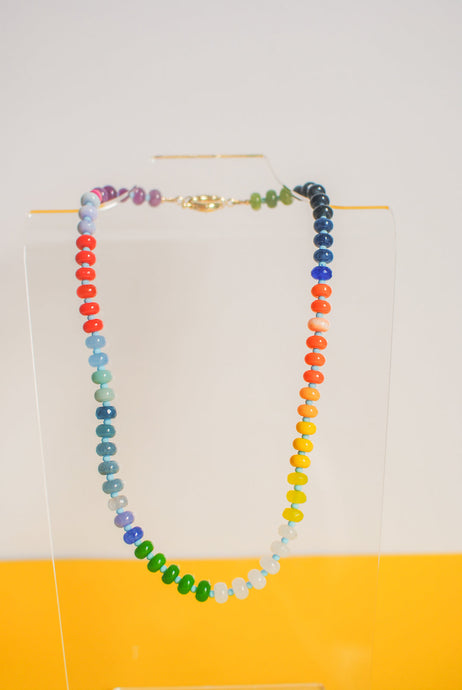 Colorful beaded necklace on a stand against a white and yellow background