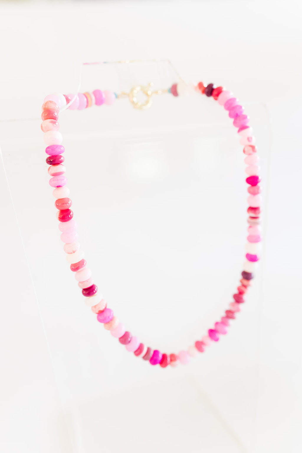 A necklace with a mix of shades of pink and white opal beads, featuring a gold-filled clasp, displayed against a white background.
