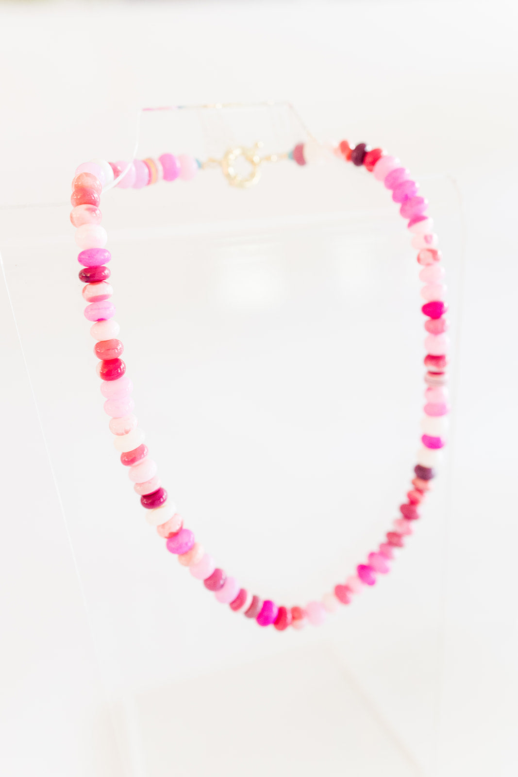 A necklace with a mix of shades of pink and white opal beads, featuring a gold-filled clasp, displayed against a white background.